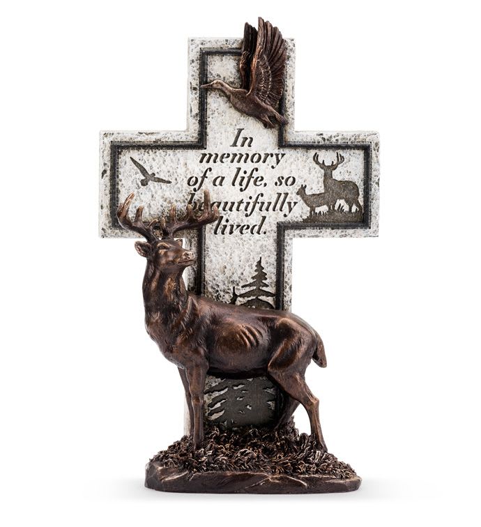 Bronze-tone deer figurine in front of a stone-look memorial cross with bird and forest silhouettes and an inscription.