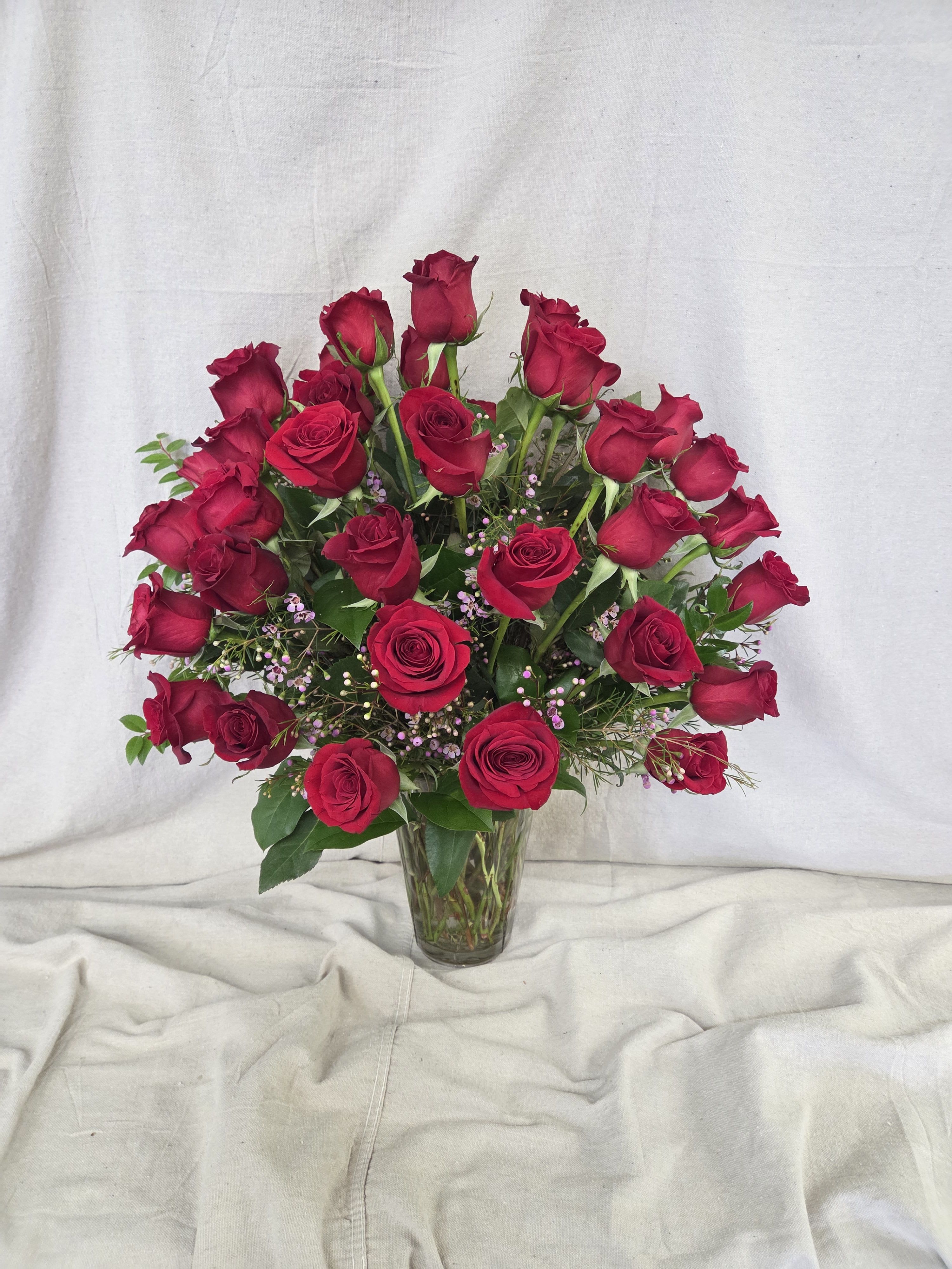Tall clear vase filled with numerous red roses and small pink filler flowers