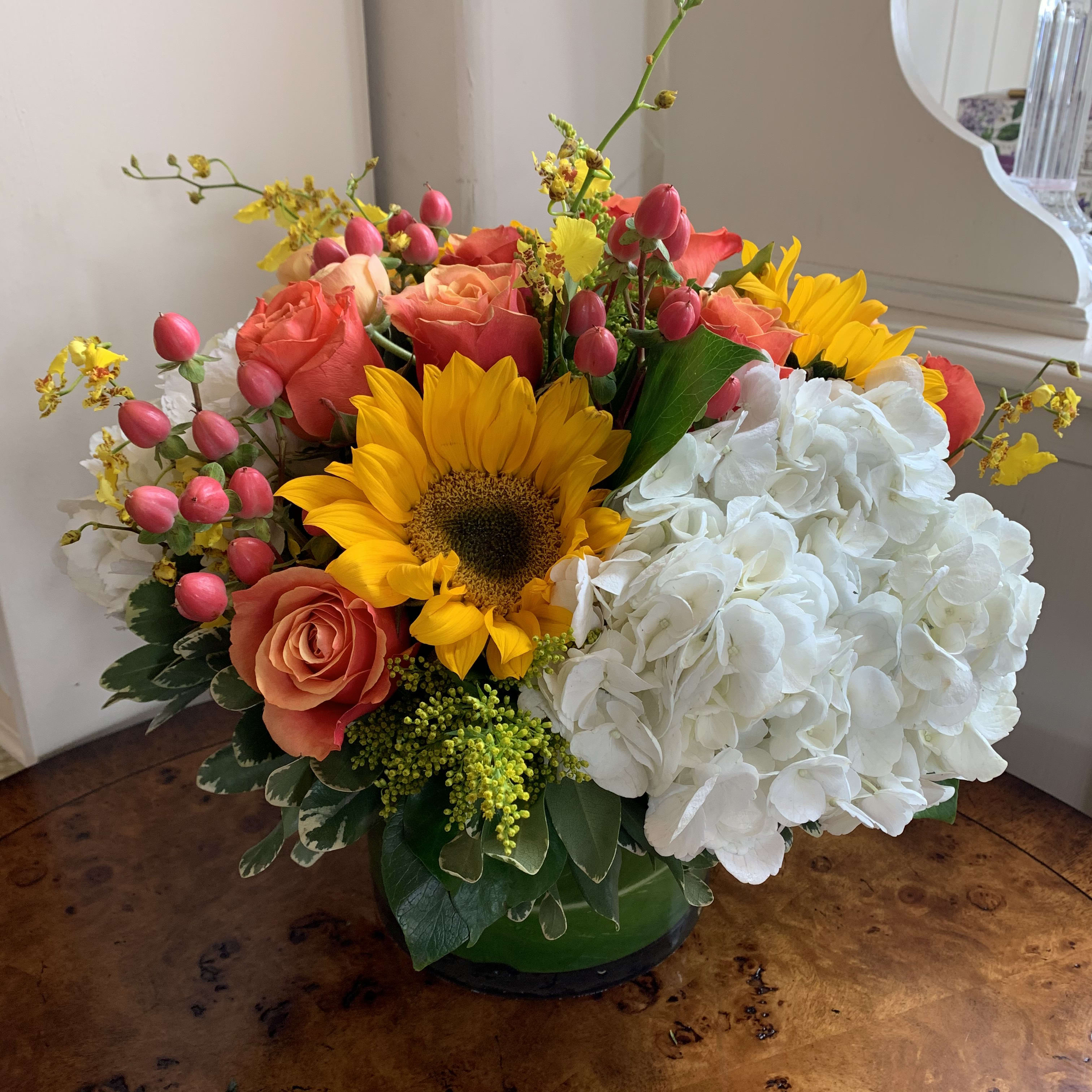 Mixed bouquet with sunflowers, coral roses, white hydrangea, and pink buds in a green vase