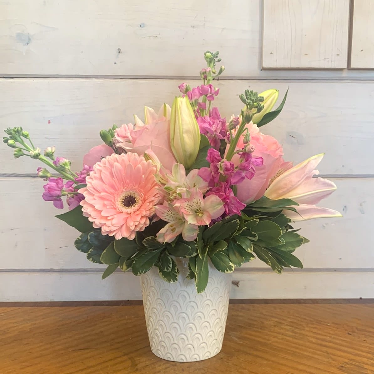 Tickled Pink - An all pink arrangement of pale pink roses, pink gerbera daisies, fragrant pink stock, and pink Asiatic lilies in a white orchid pot with pink mini carnations, and pink alstroemeria. Approximately 10" by 10".