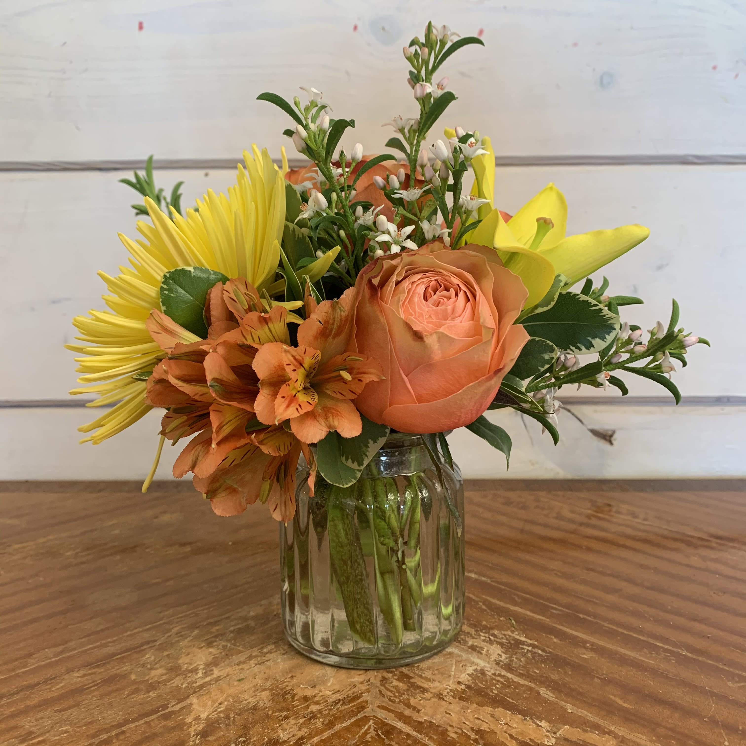 Mixed bouquet of orange, yellow, and white flowers in a glass jar