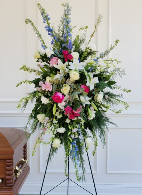Tall standing floral spray with pink, white, and blue blooms on a black easel