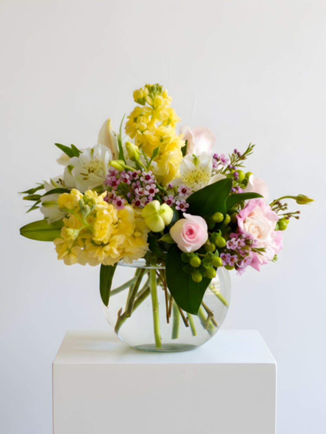 Mixed bouquet of yellow, pink, and white flowers in a clear glass vase.