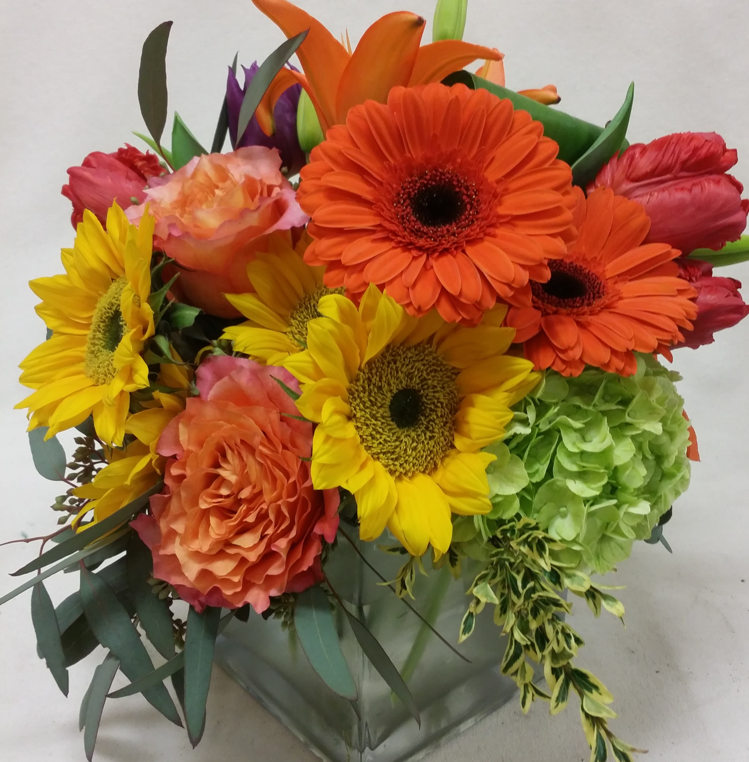 Bright mixed bouquet with sunflowers, gerbera daisies, roses, and hydrangea in a glass vase