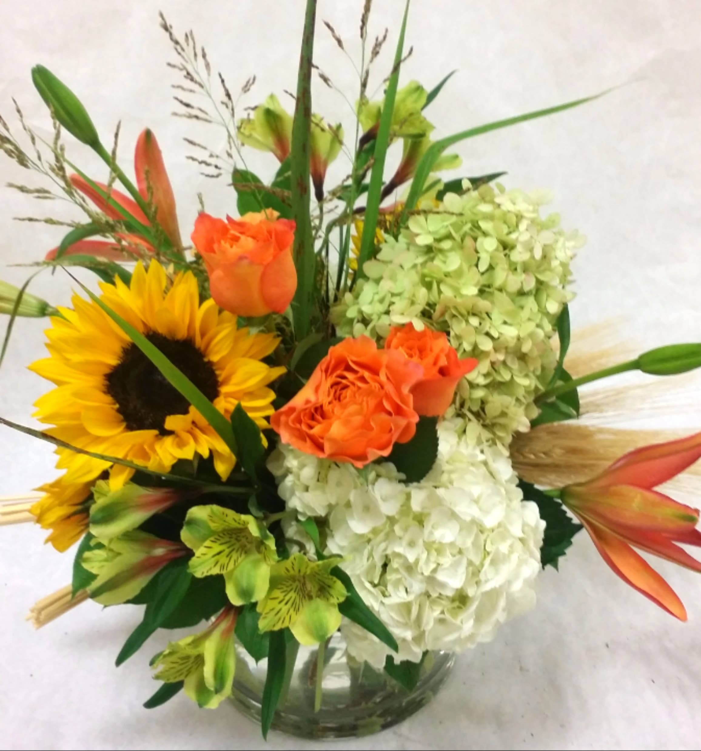 Bouquet with sunflowers, orange roses, white hydrangeas, and lilies in a glass vase