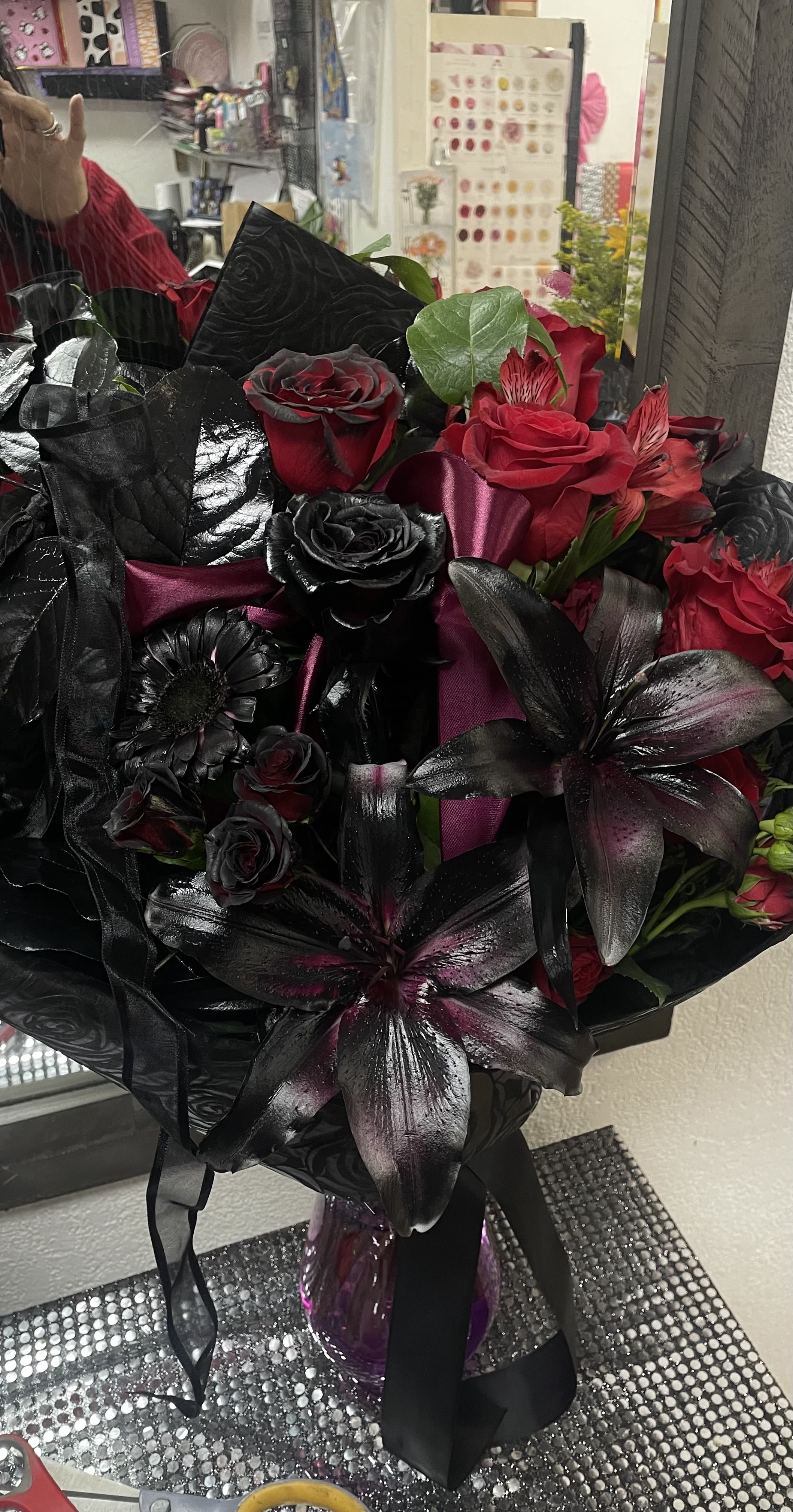 Bouquet of red and black roses with dark lilies in a glass vase