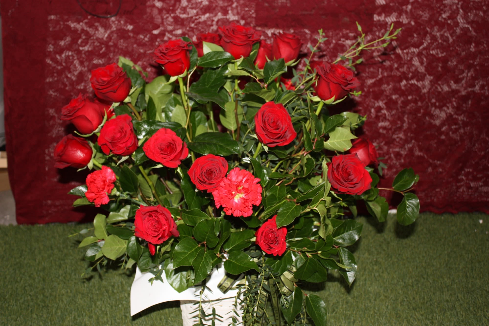 Arrangement of red roses with a few red carnations in a white basket against a burgundy background
