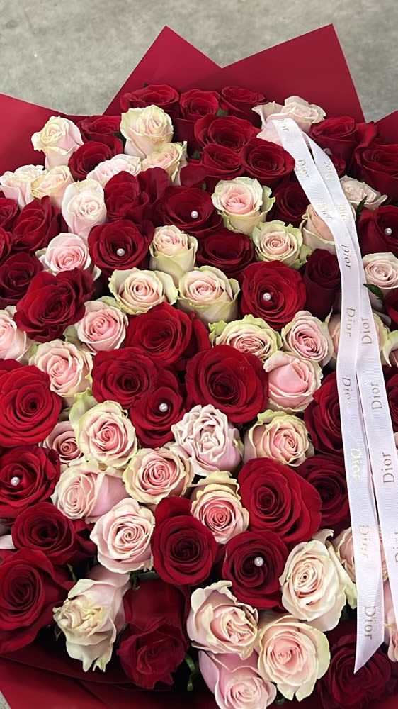 100 pink red white - A lush, oversized bouquet of red, pink and white roses creates an immediate sense of romance and celebration-the perfect birthday bouquet, anniversary roses, or Mother's Day gift that makes the person you're thinking of feel truly adored. The dense, plush arrangement reads as a single luxurious bloom from afar, then reveals itself up close: deep crimson roses melt into soft blush and cream-toned roses for a rich color gradient that feels both classic and modern. Small pearl pins tucked into several red blooms add a jewel-like sparkle that catches the light and lifts the design.  Wrapped in layered red paper and finished with a white designer ribbon, this arrangement arrives ready to present for weddings, Valentine's Day, prom, or a heartfelt "I'm sorry" or "Thinking of you" moment. The bouquet's generous size gives it strong visual impact for sympathy and funeral settings as well as joyful occasions like graduation, housewarming, or a new baby celebration. For best results, recut stems at an angle and place in fresh water with flower food upon arrival to keep the roses looking hydrated and luxurious.