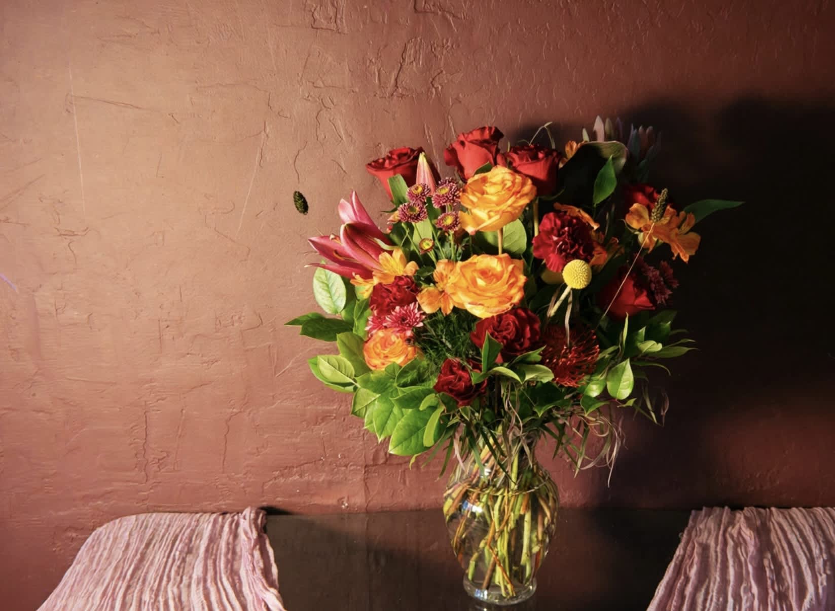 Mixed bouquet of red, orange, and pink flowers in a clear glass vase