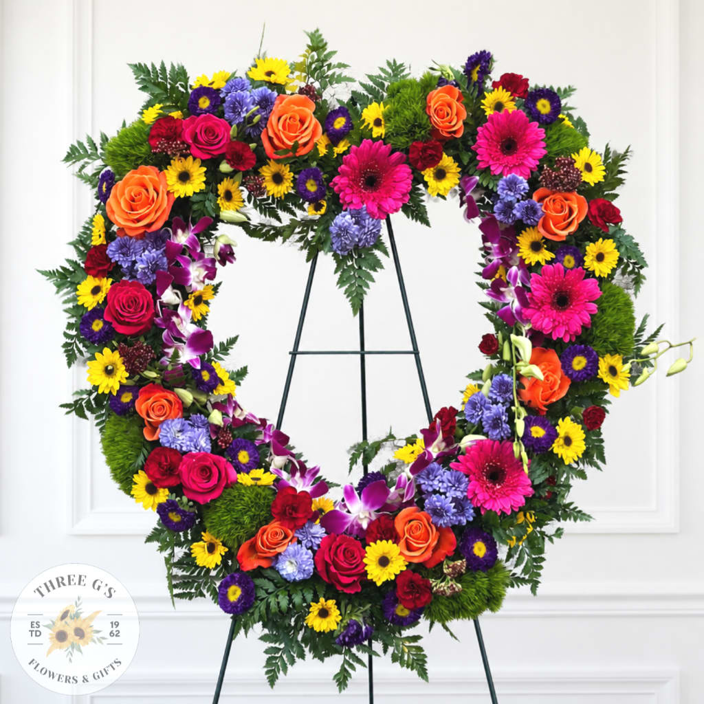 Heart-shaped floral wreath with roses, daisies, and orchids on an easel