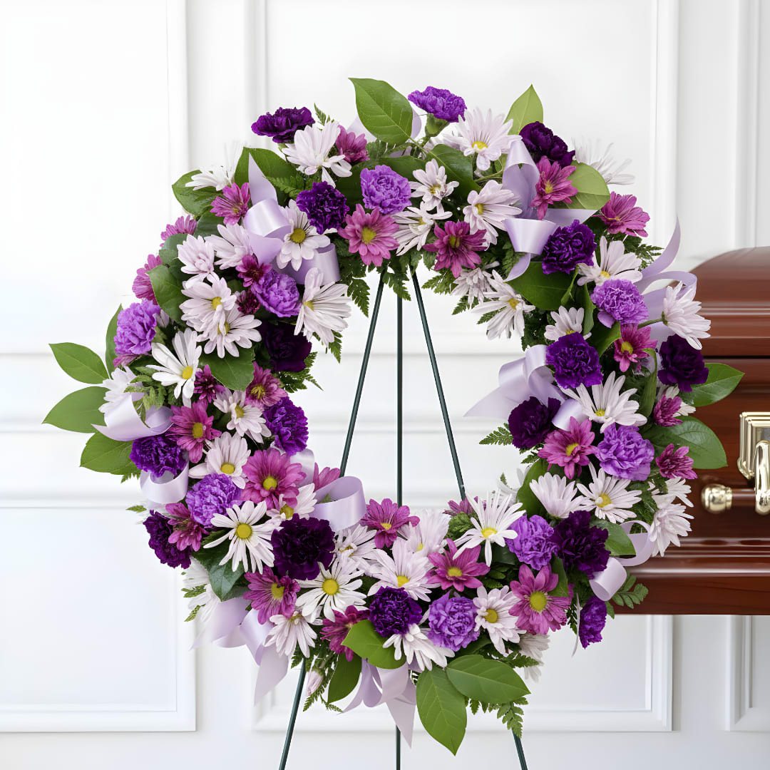 Purple and white floral wreath on a stand beside a casket