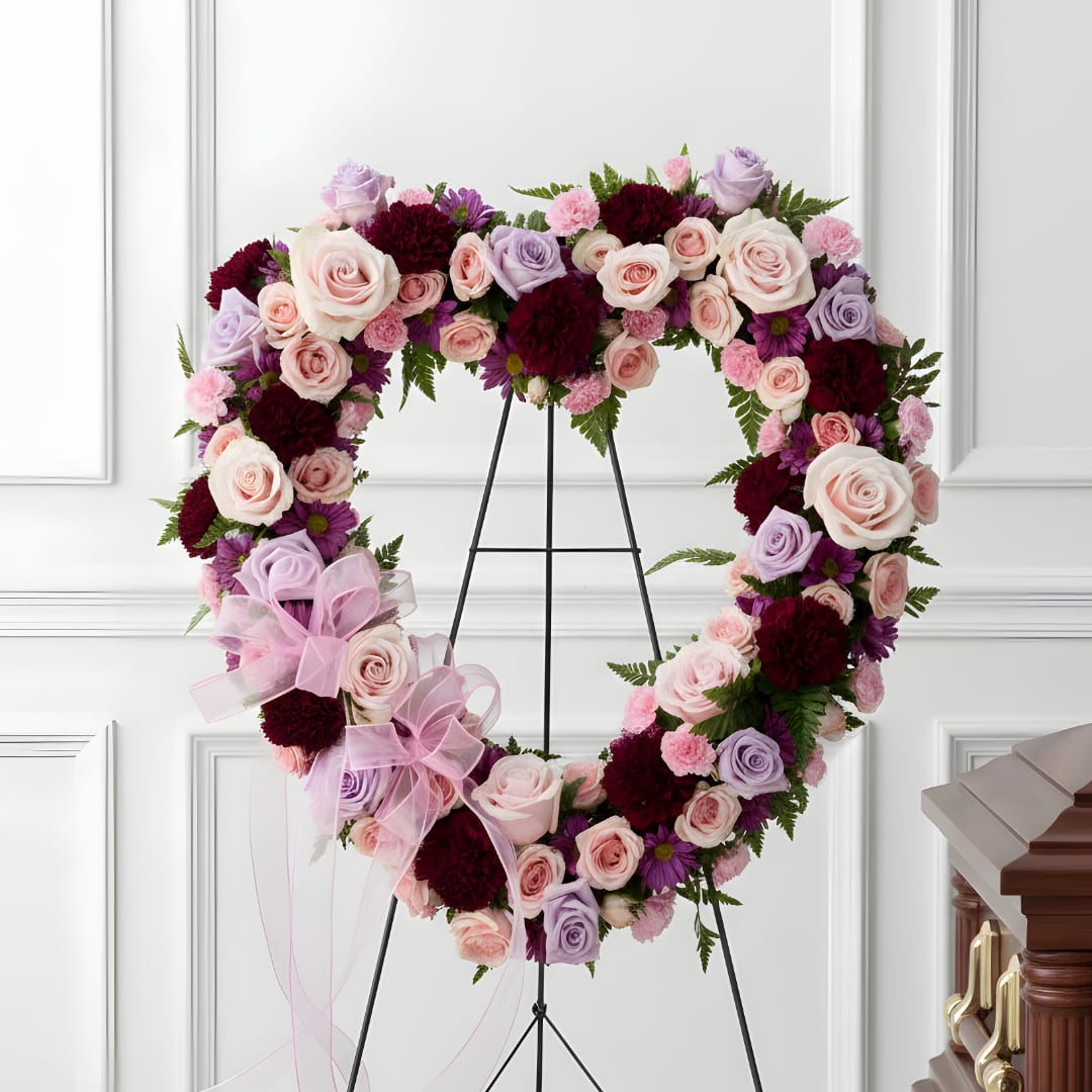 Heart-shaped floral wreath on a stand with pink, lavender, and burgundy flowers