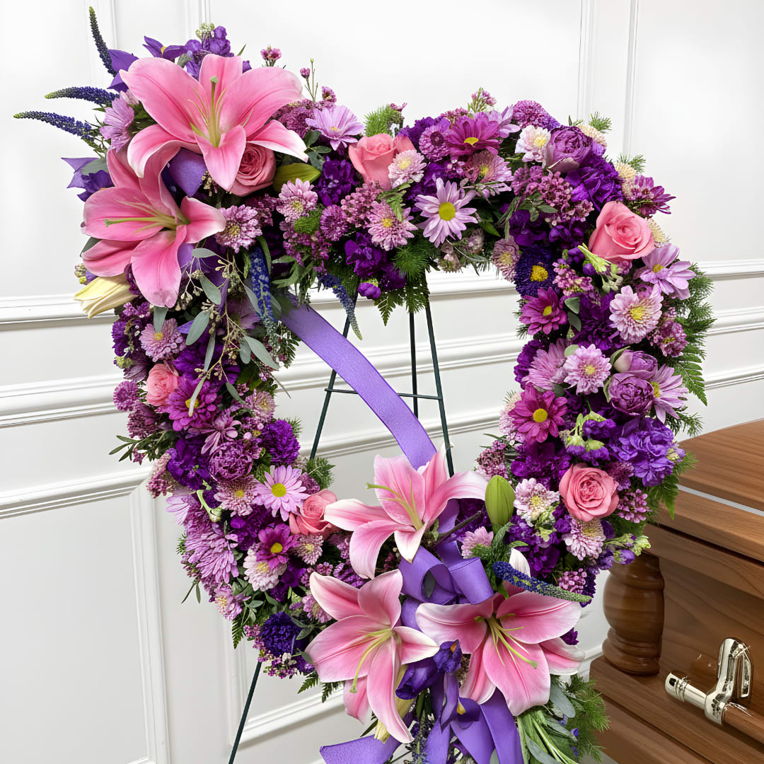 Heart-shaped floral wreath with pink lilies and purple flowers on a stand