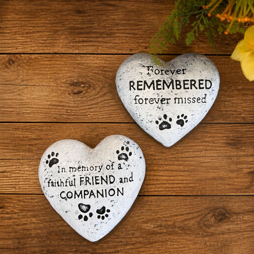 Two heart-shaped memorial stones with paw prints and text on a wooden surface.