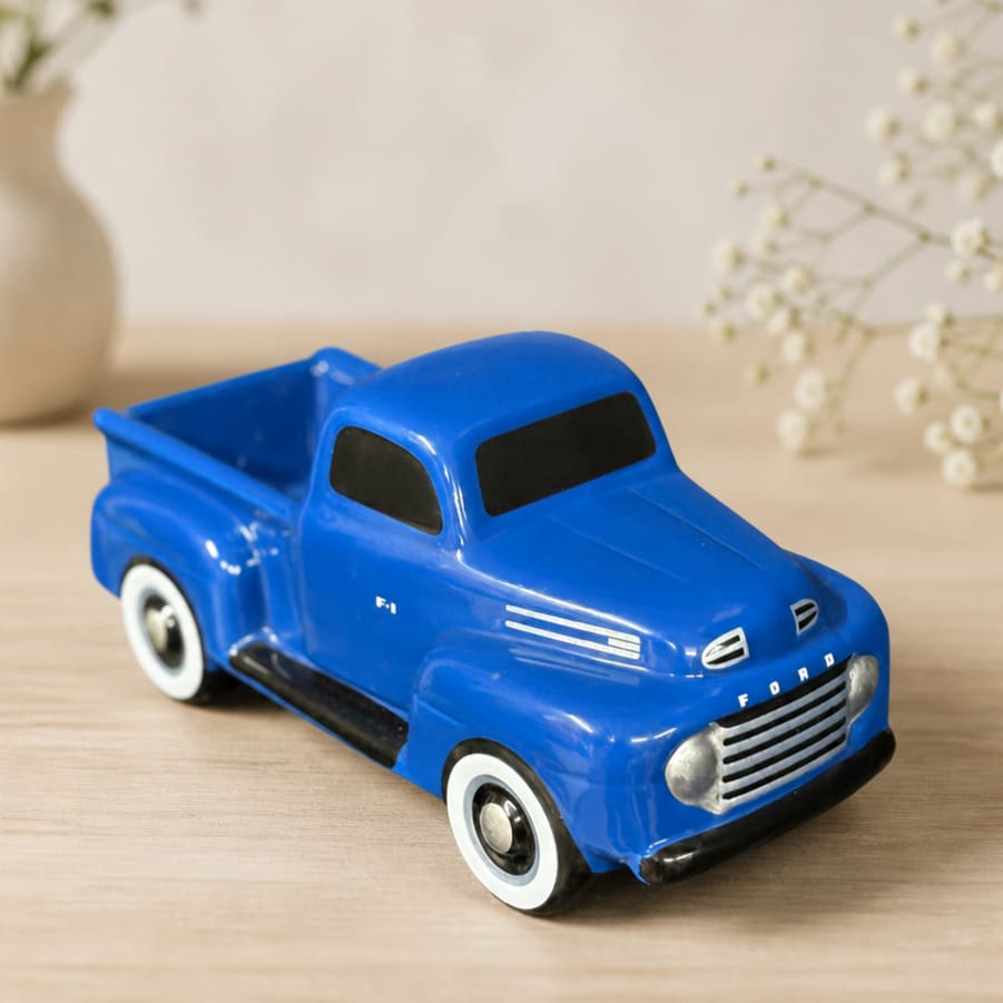 Blue toy pickup truck on a wooden surface with blurred white flowers in the background