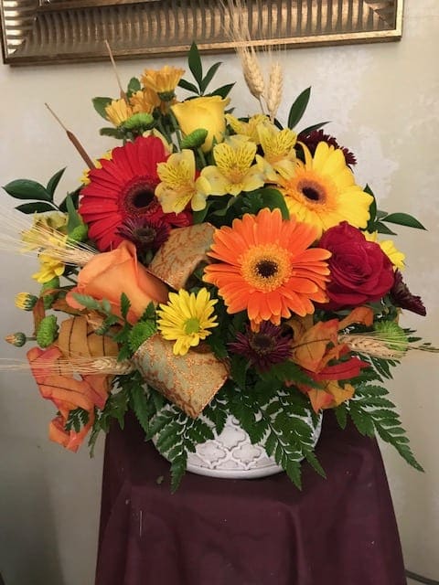 SUNSET IN STONE ARRANGEMENT - A DECORATIVE STONE CONTAINER, FILLED WITH BRIGHT FALL FLOWERS, WHEAT AND COLORFUL LEAVES.