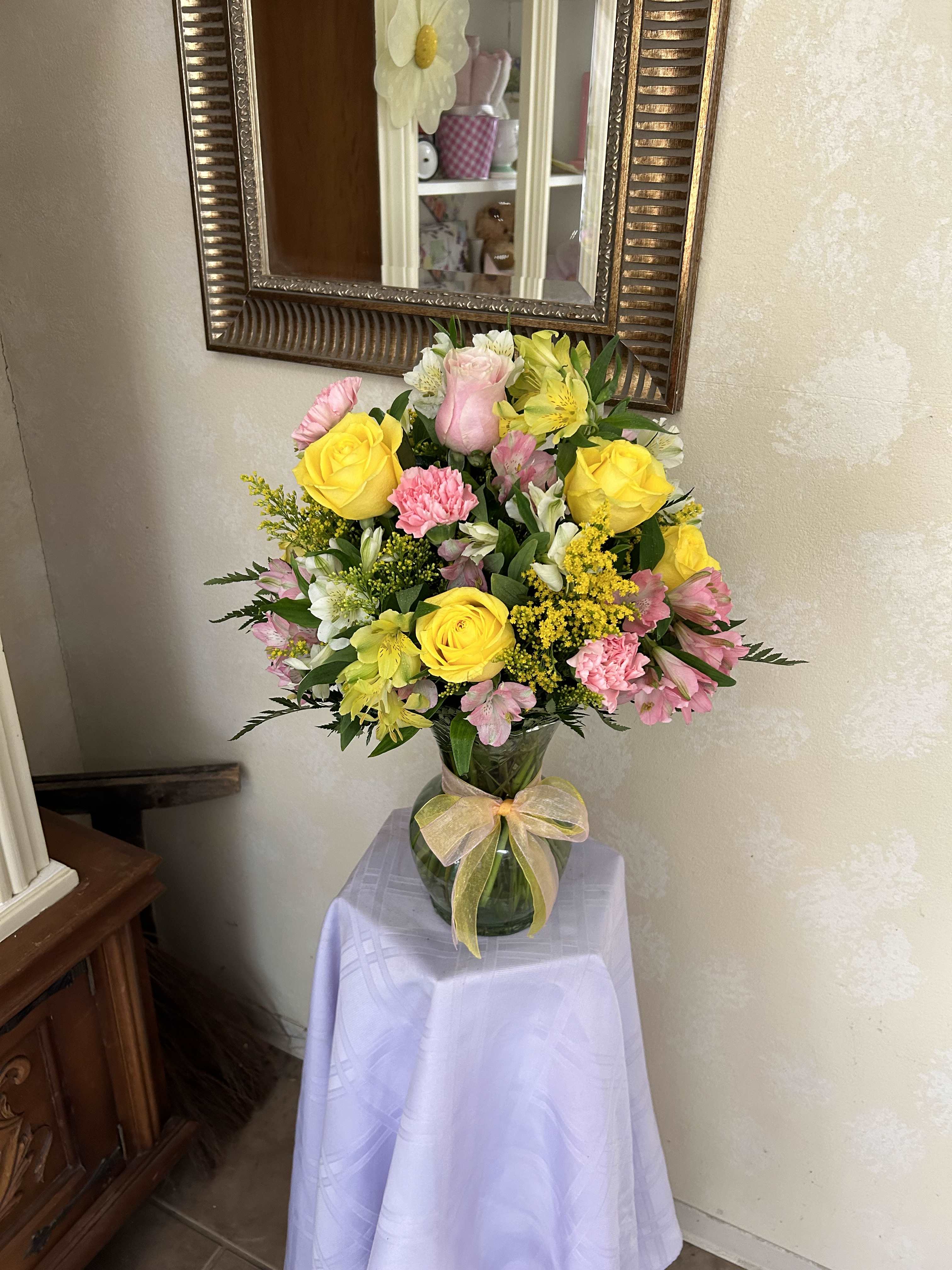Mixed bouquet of yellow roses, pink carnations, and white flowers in a glass vase