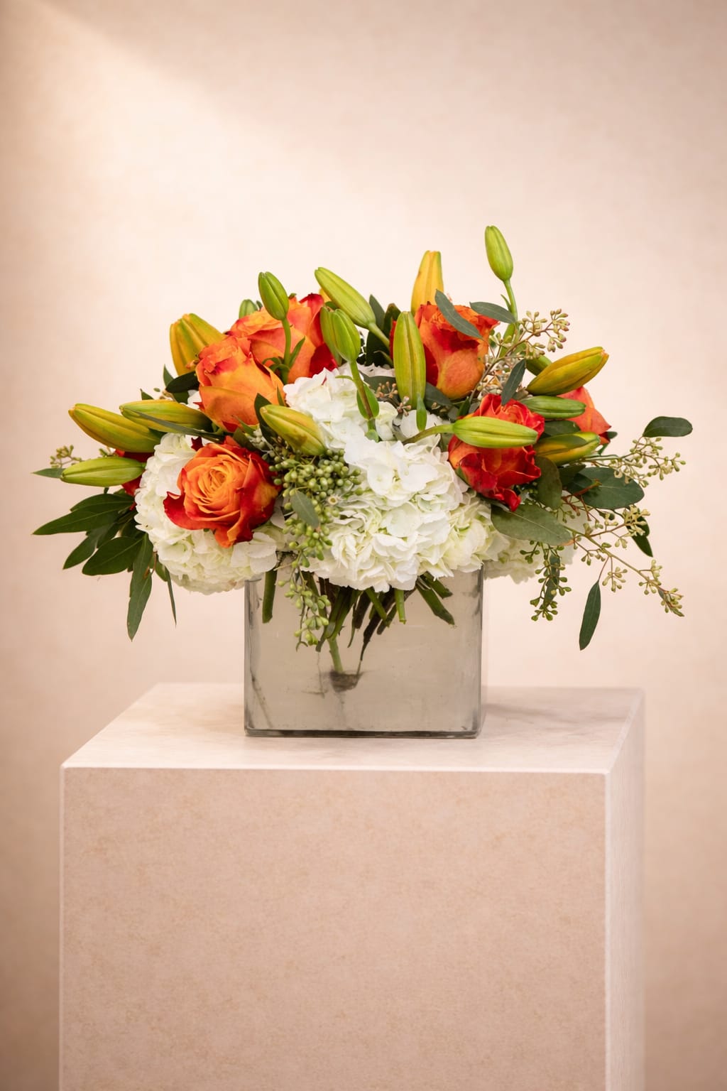Low glass vase arrangement with orange roses, white hydrangeas, and green lily buds.