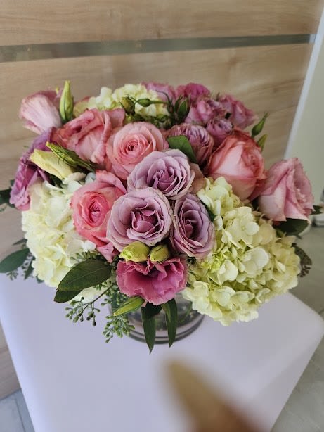 Low bouquet of pink roses, lavender lisianthus, and white hydrangeas in a clear glass vase