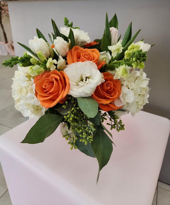 Compact bouquet of orange roses and white blooms in a clear glass vase