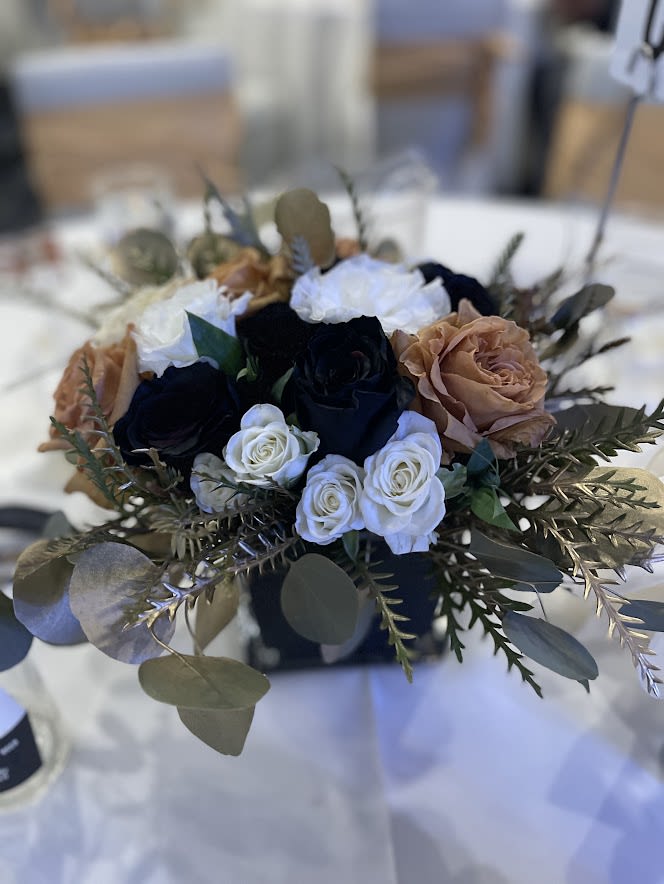 Low centerpiece of white, tan, and dark roses in a black square vase