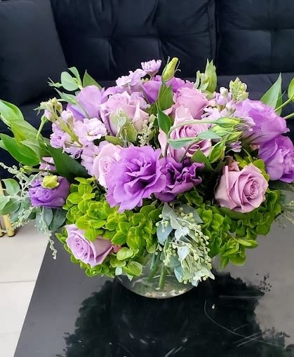Low round arrangement of purple and lavender flowers in a clear glass bowl vase