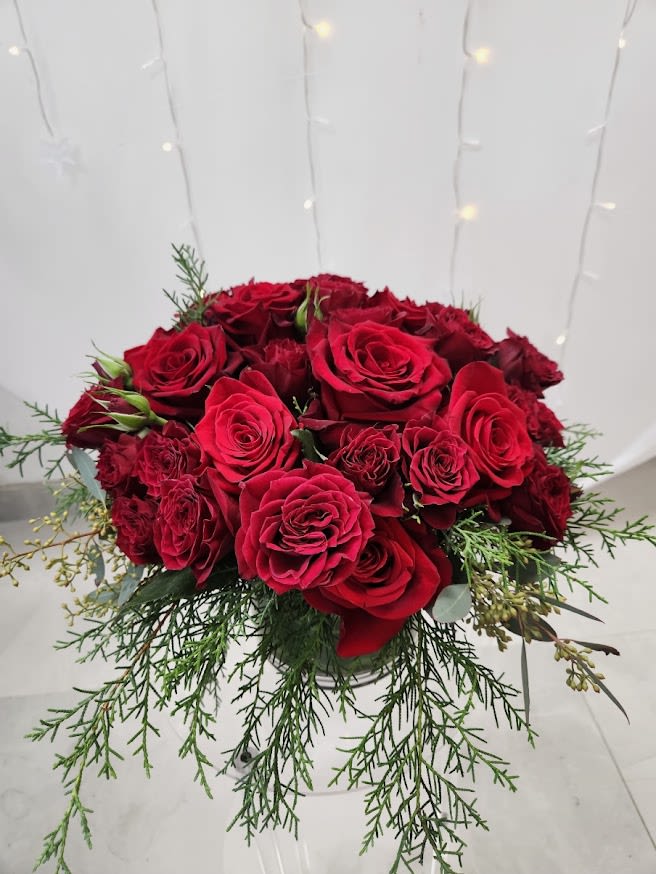 Compact arrangement of red roses in a glass vase with trailing evergreen accents