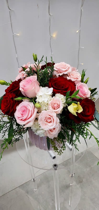 Round arrangement of red and pale pink roses with white blooms in a pink glass vase