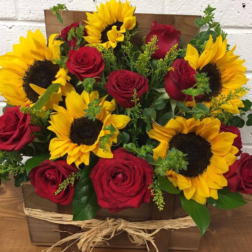 Bouquet of red roses and yellow sunflowers in a wooden box