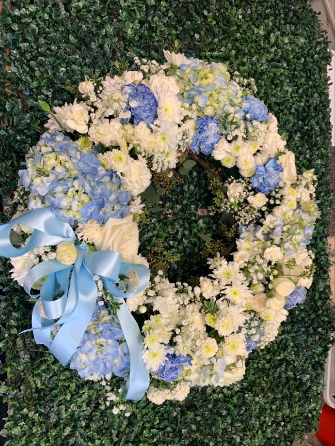 Heart-shaped floral wreath with blue and white flowers and a light blue ribbon