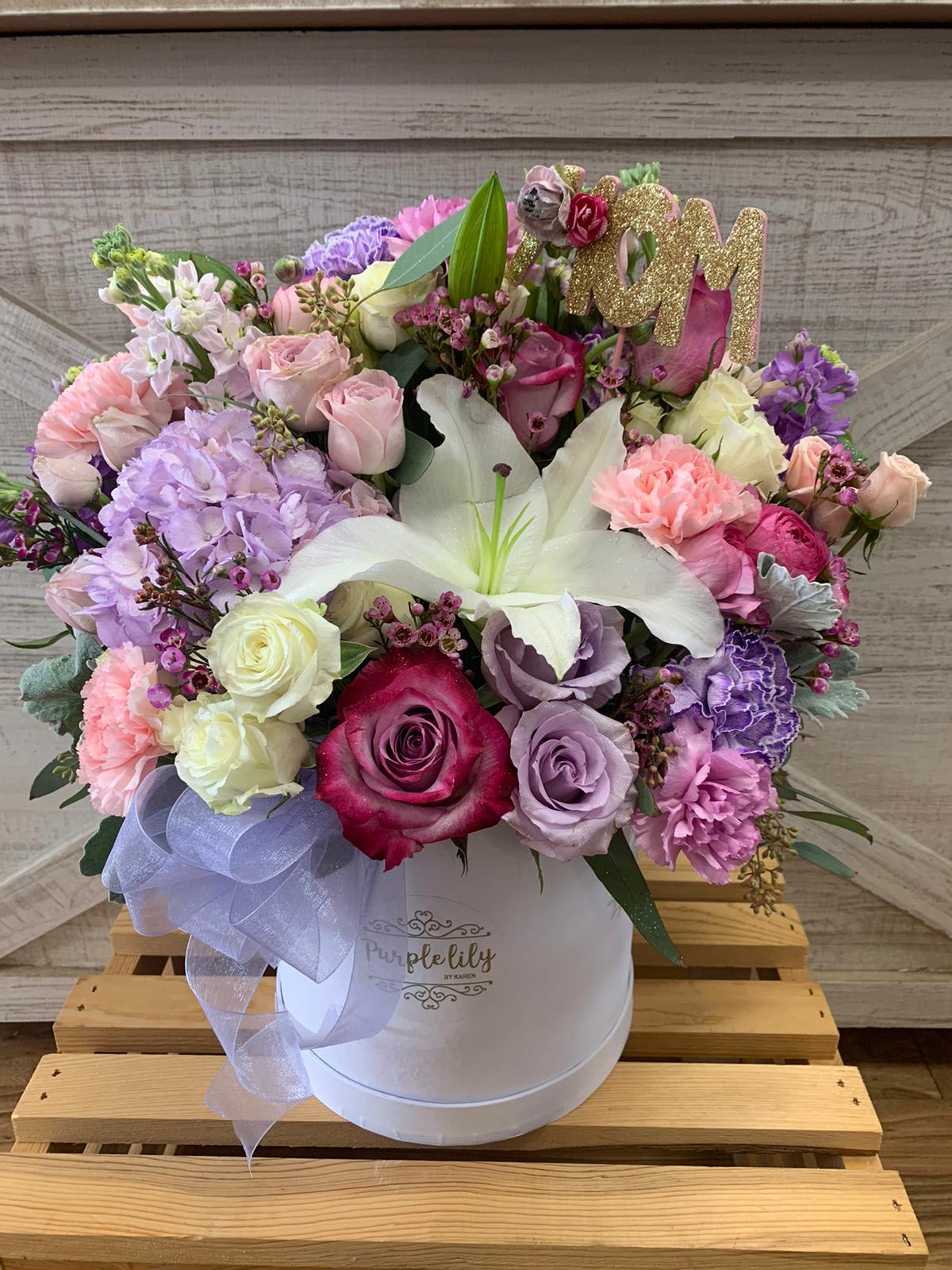 Pastel bouquet of roses, lilies, and carnations in a white hat box with a glittery "M" topper