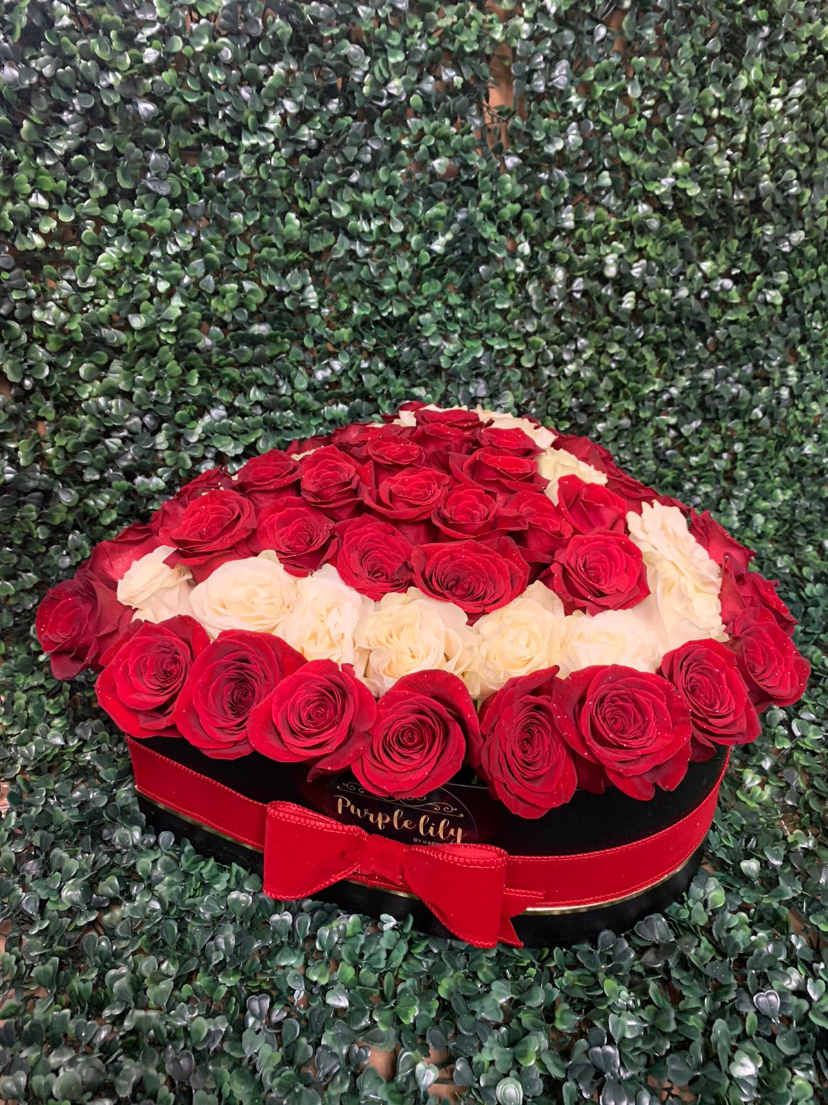 Red and cream roses arranged in a round black box with a red ribbon