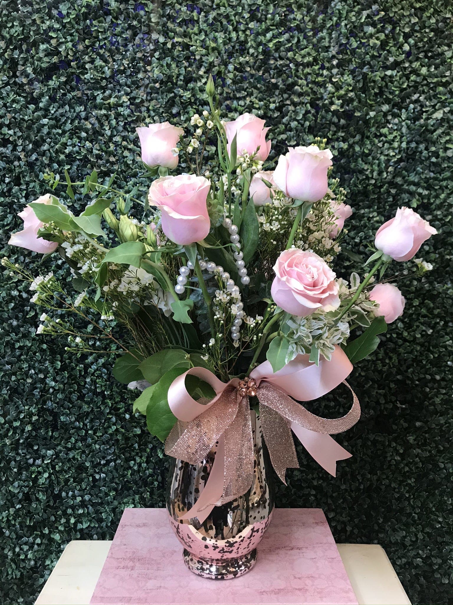 Pink roses arranged in a patterned vase with a pink ribbon bow