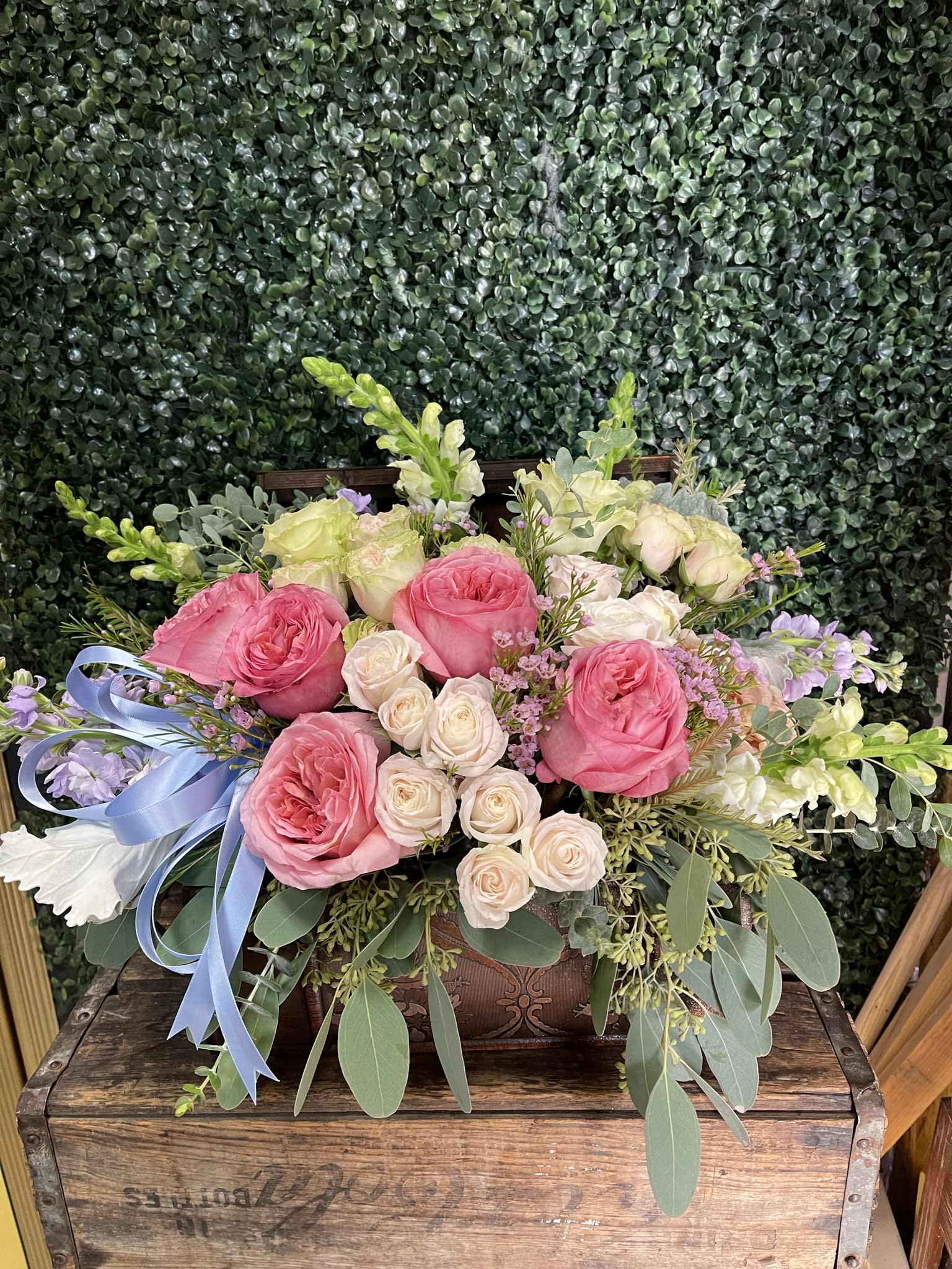 Pink and cream roses arranged in a wooden box with a blue ribbon