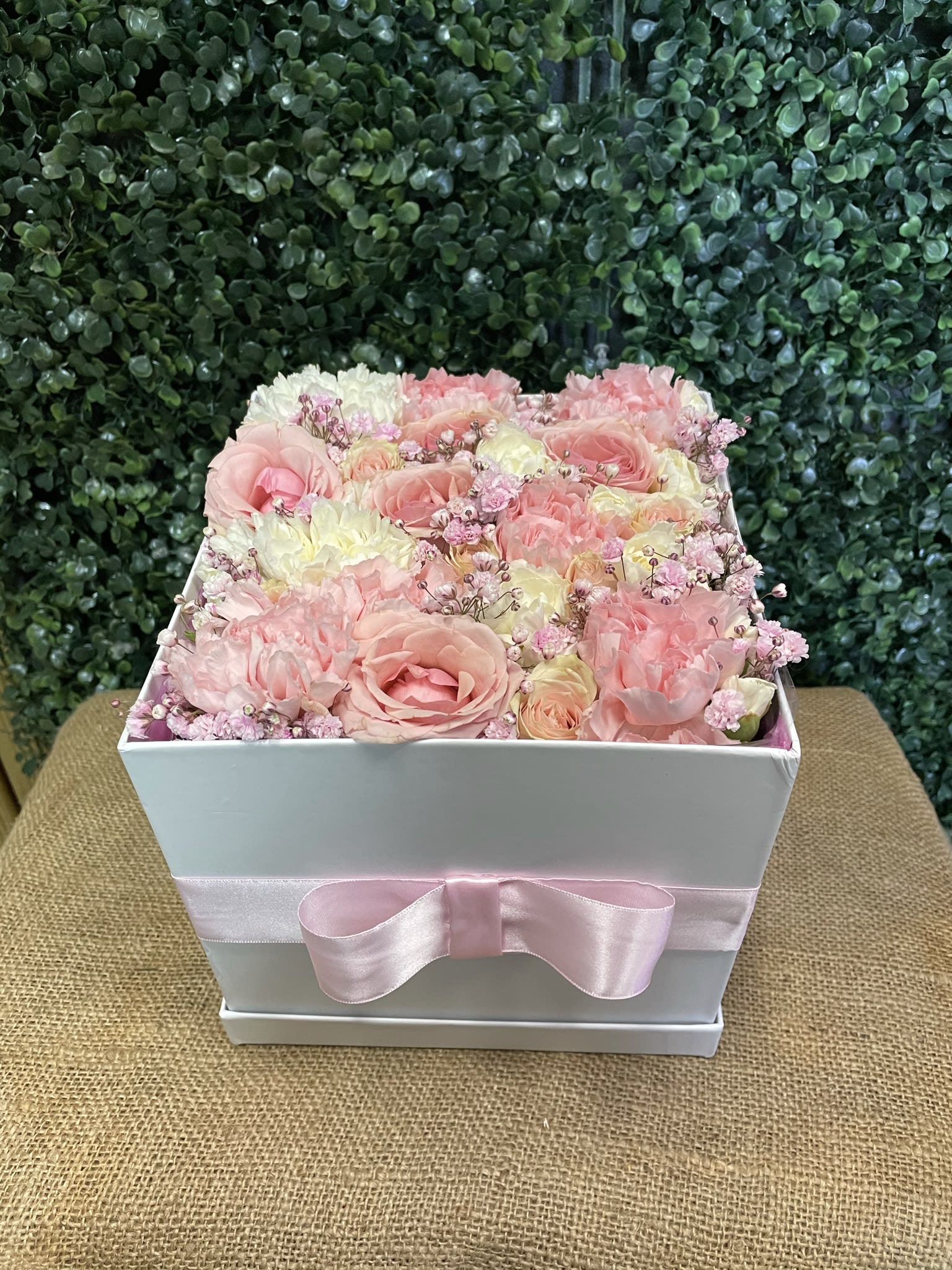 Pink and white roses arranged in a white box with a pink ribbon