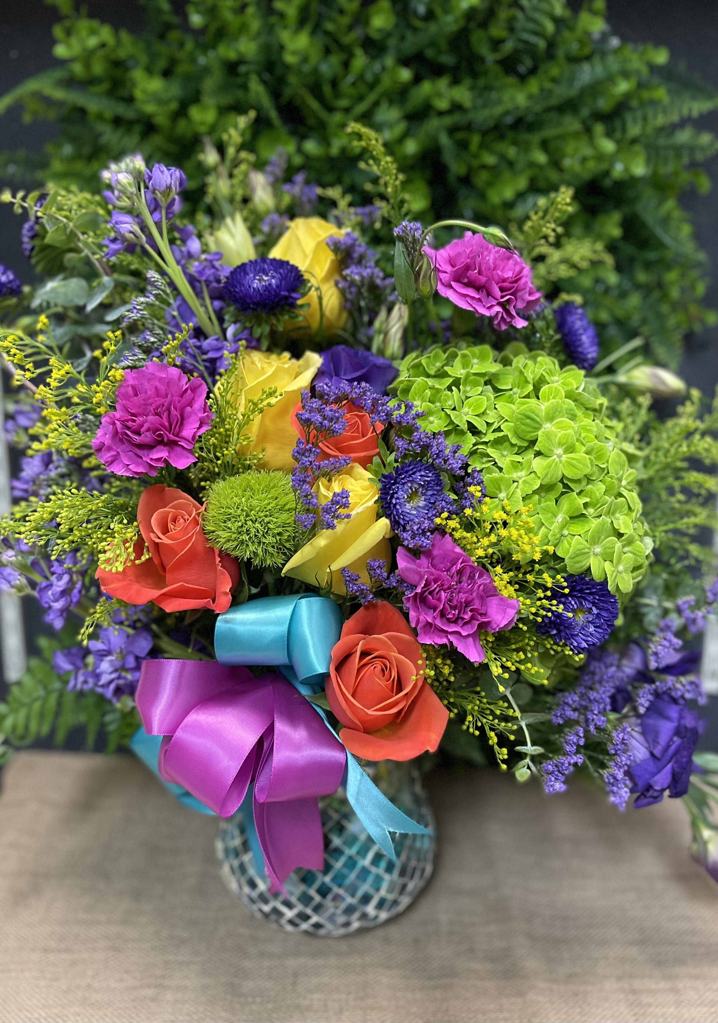 Colorful bouquet of roses, carnations, and purple blooms in a patterned vase