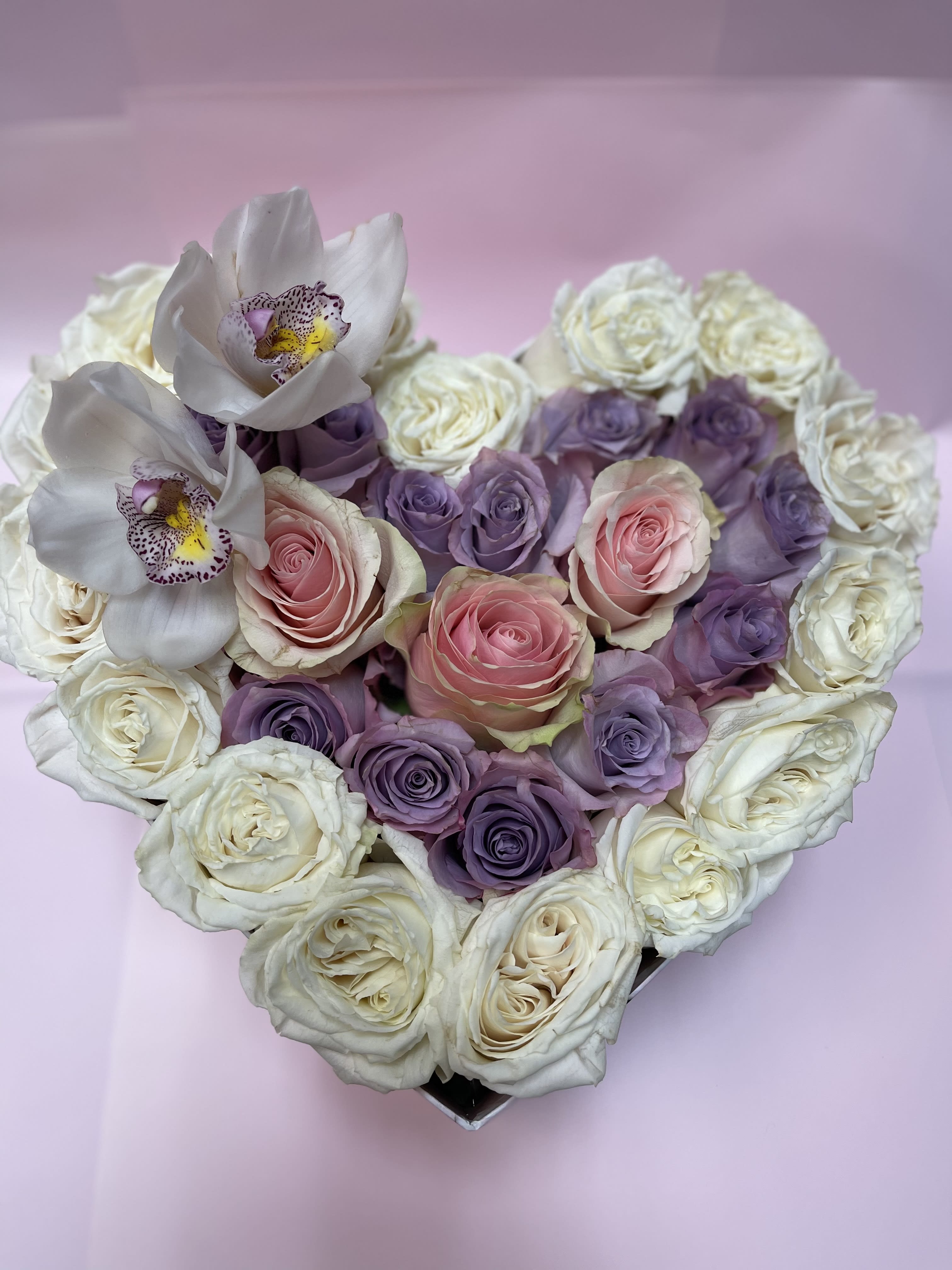 Heart-shaped bouquet of pink, purple, and white roses with white orchids