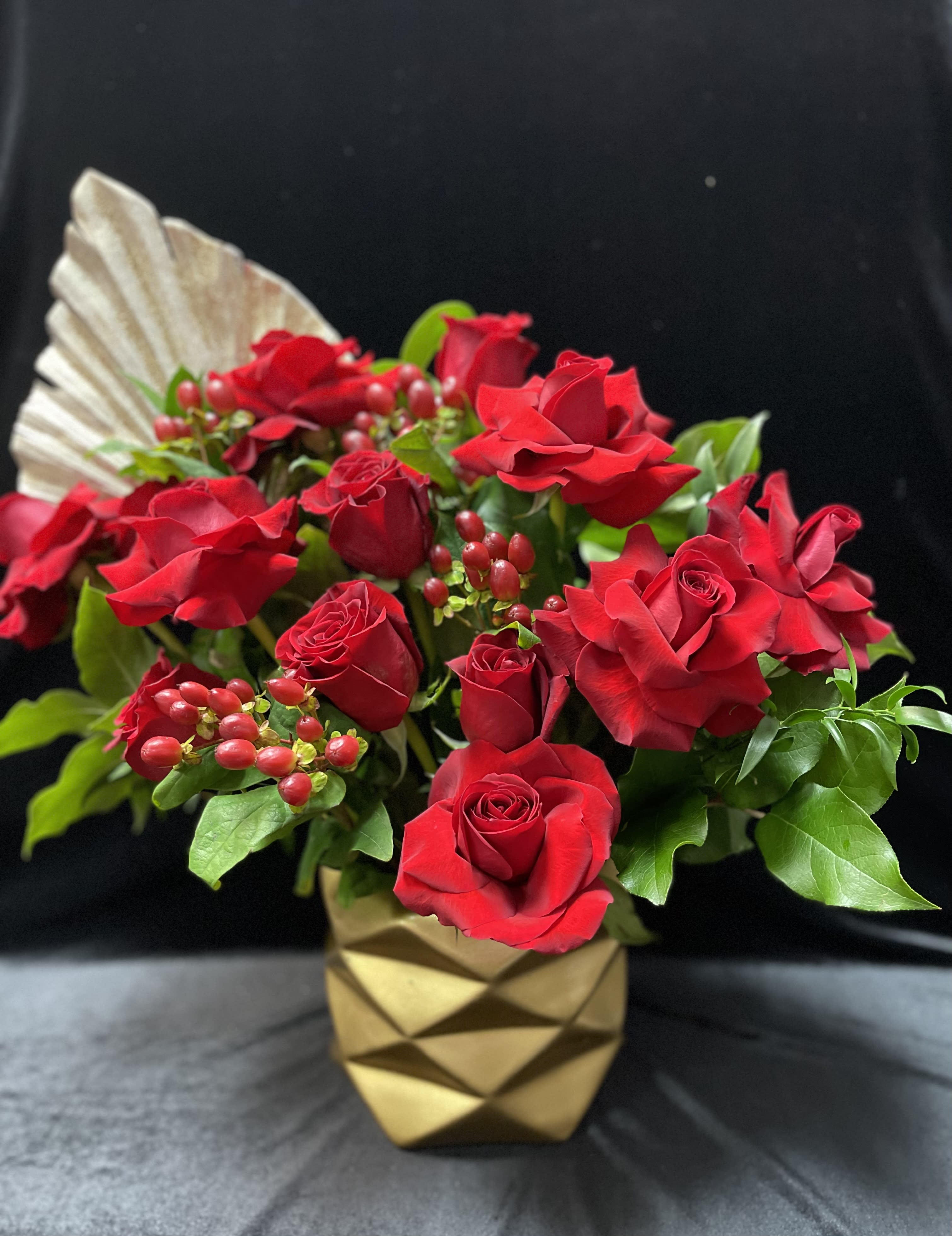 Red roses arranged in a gold geometric vase with berry accents