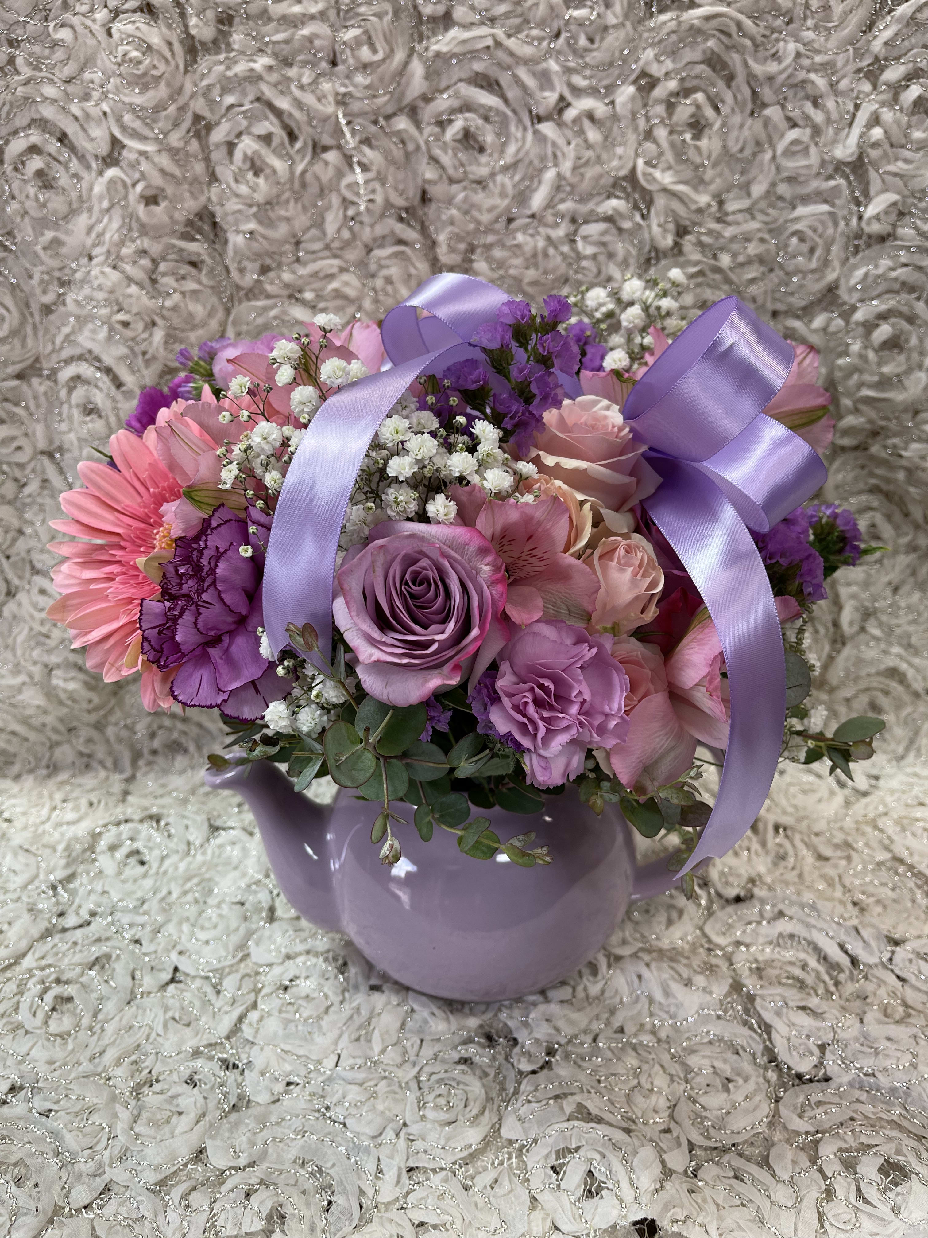Pink and purple flower arrangement in a lavender teapot vase with ribbon