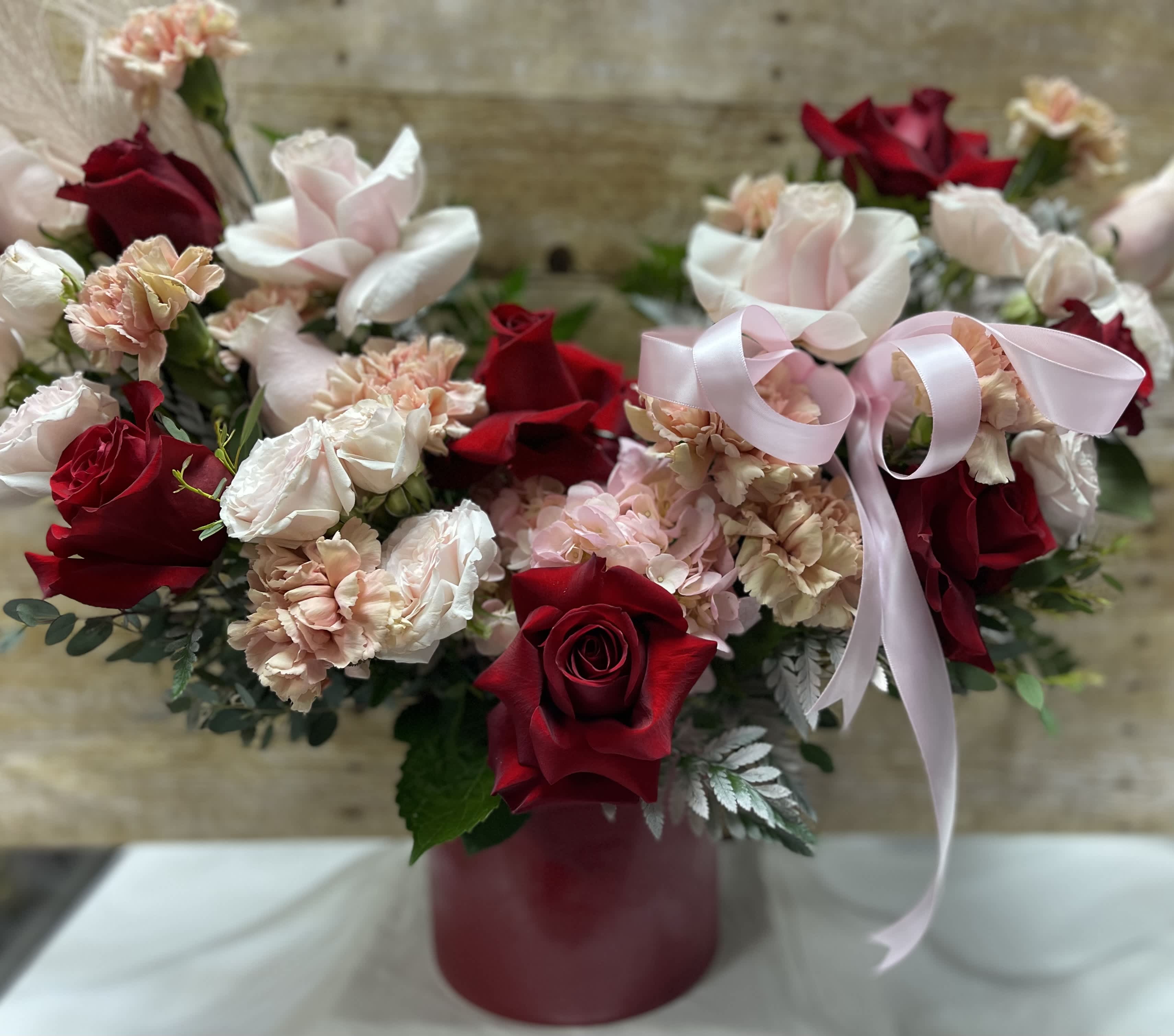 Red roses and pale pink carnations in a burgundy vase with a pink ribbon