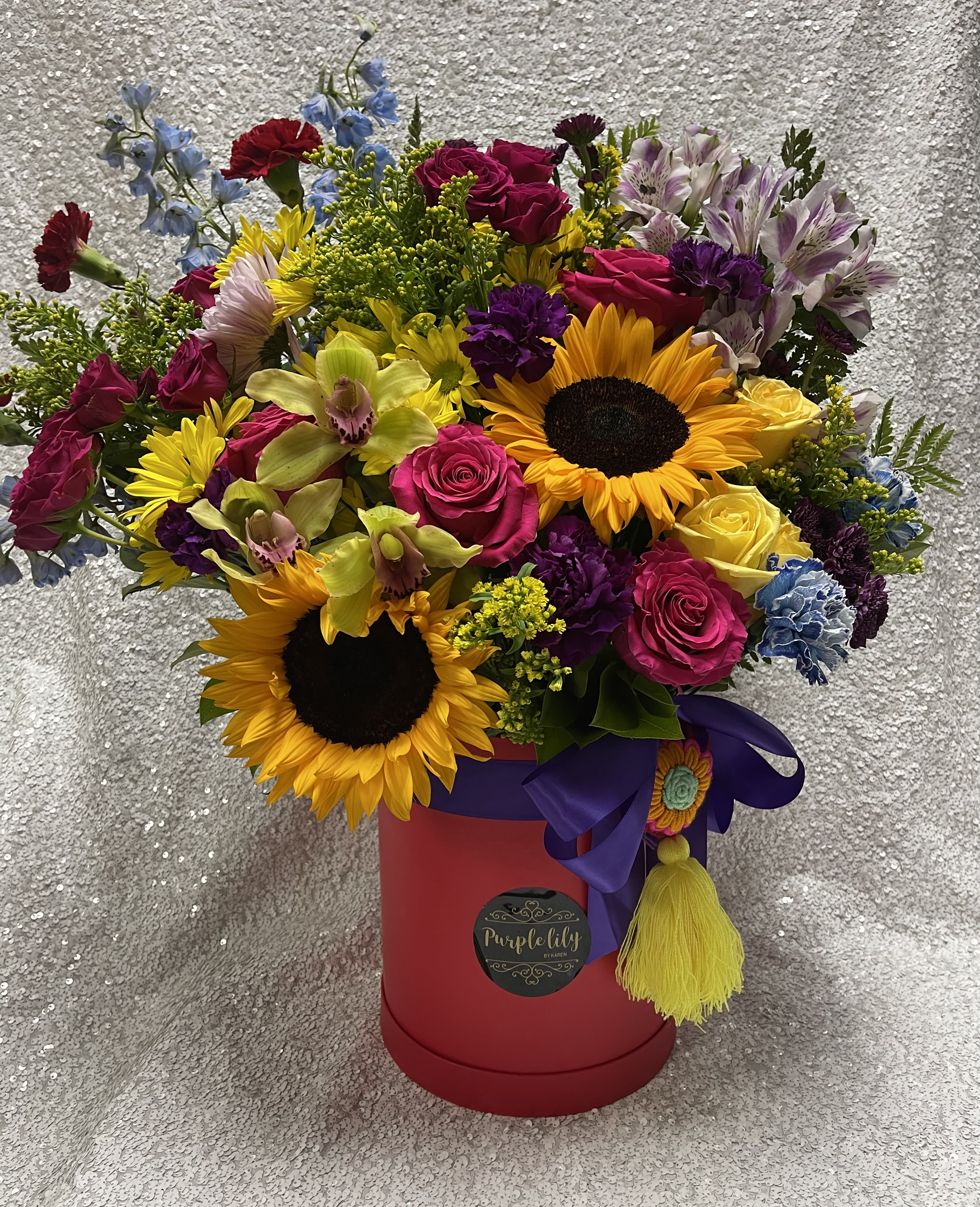 Mixed bouquet with sunflowers, roses, orchids, and alstroemeria in a red hatbox