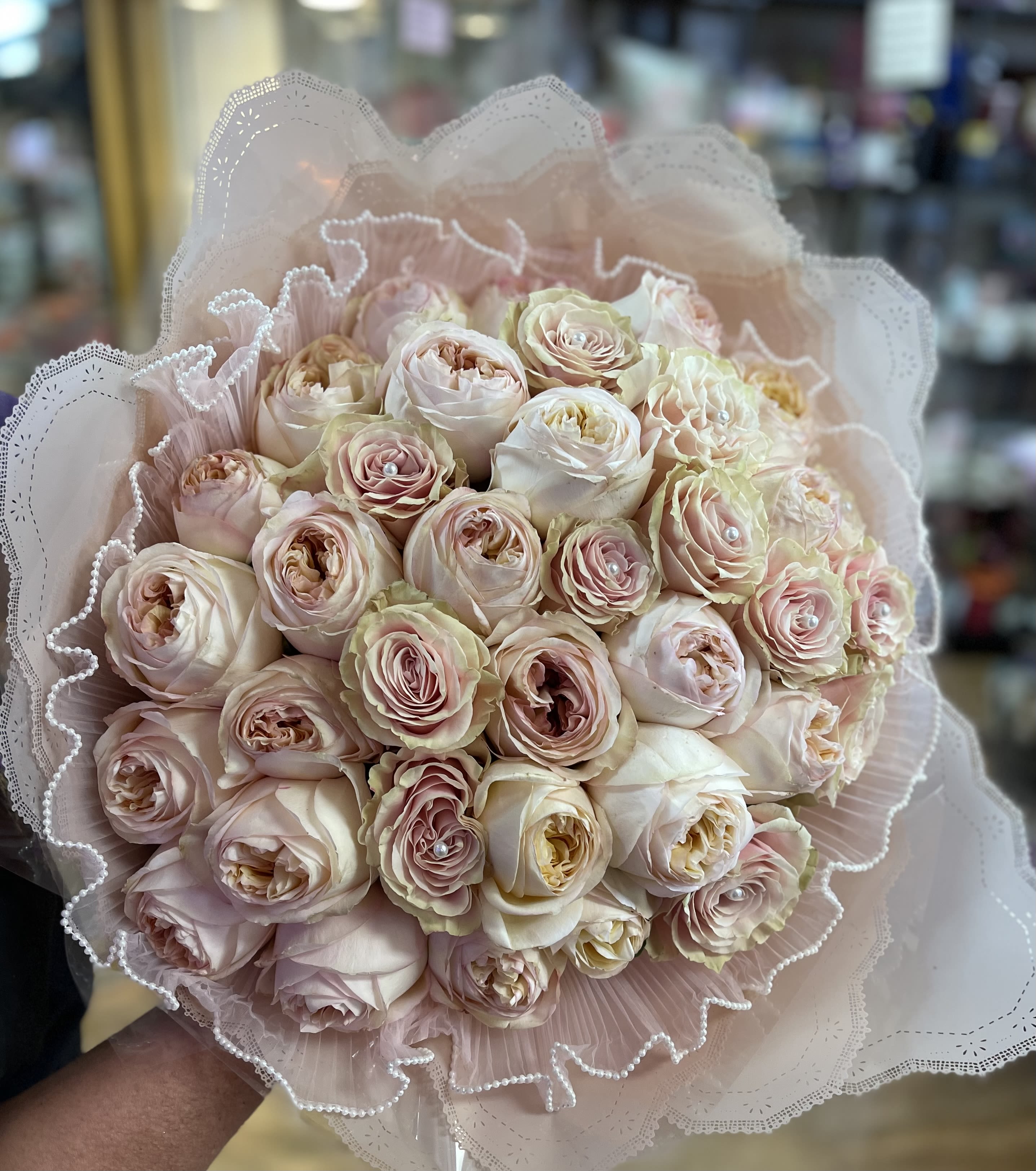 Bouquet of pale pink and cream roses wrapped in lace-like paper