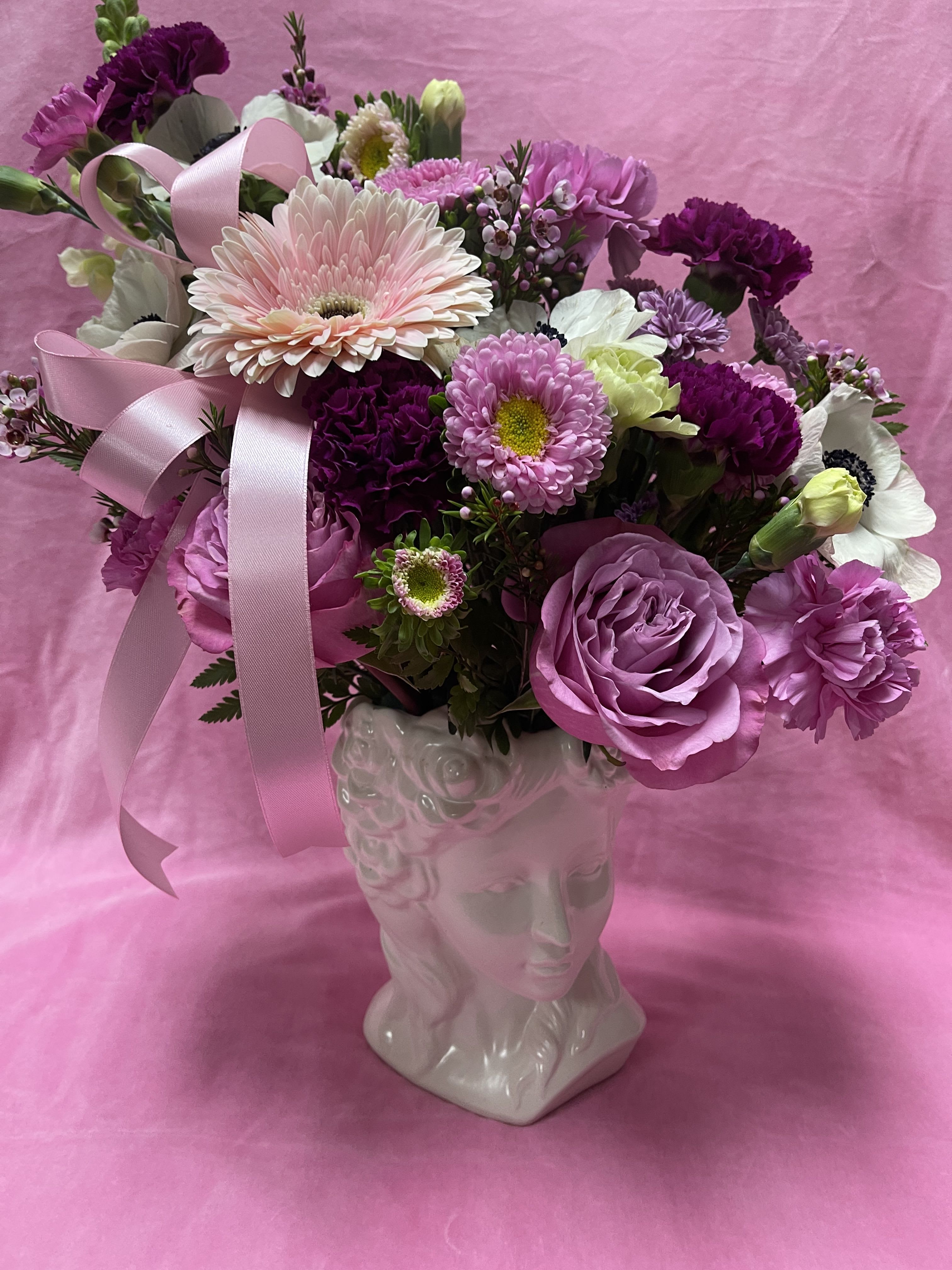 Pink and purple flower arrangement in a white face vase with ribbon