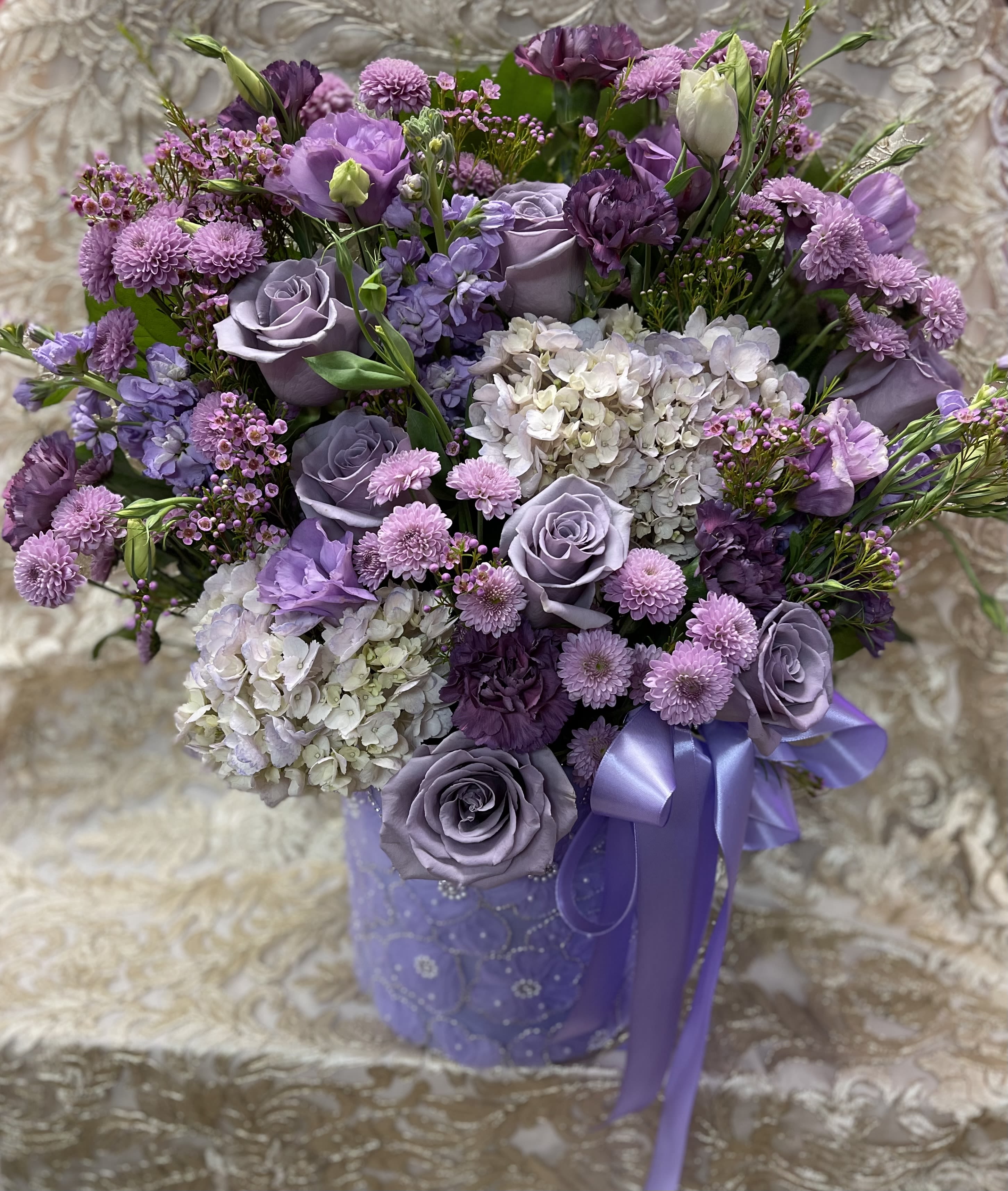 Lavender and purple bouquet with roses, hydrangeas, and ribbon in a purple vase