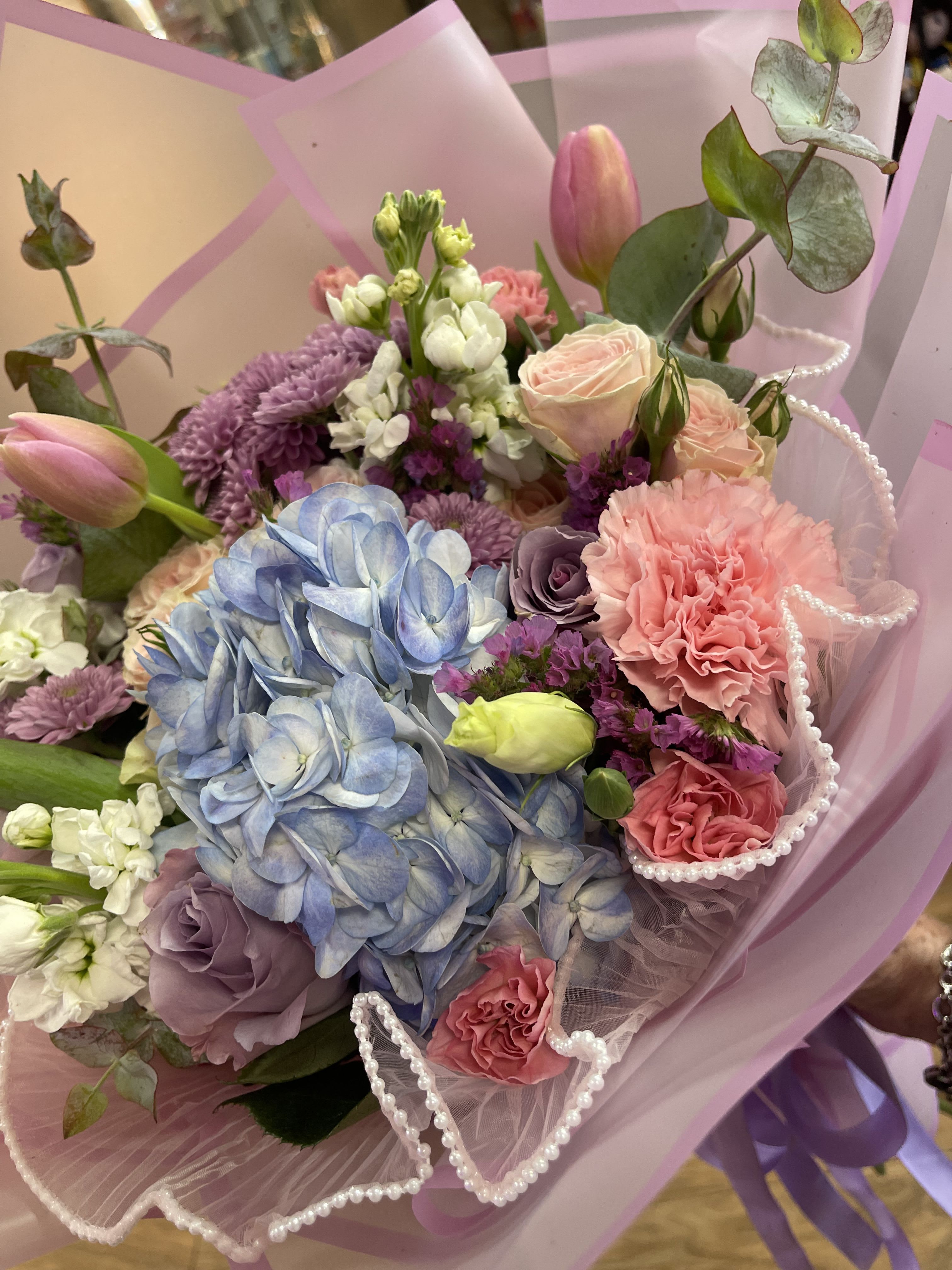 Pastel bouquet with blue hydrangea, pink roses, and purple blooms in pink wrap