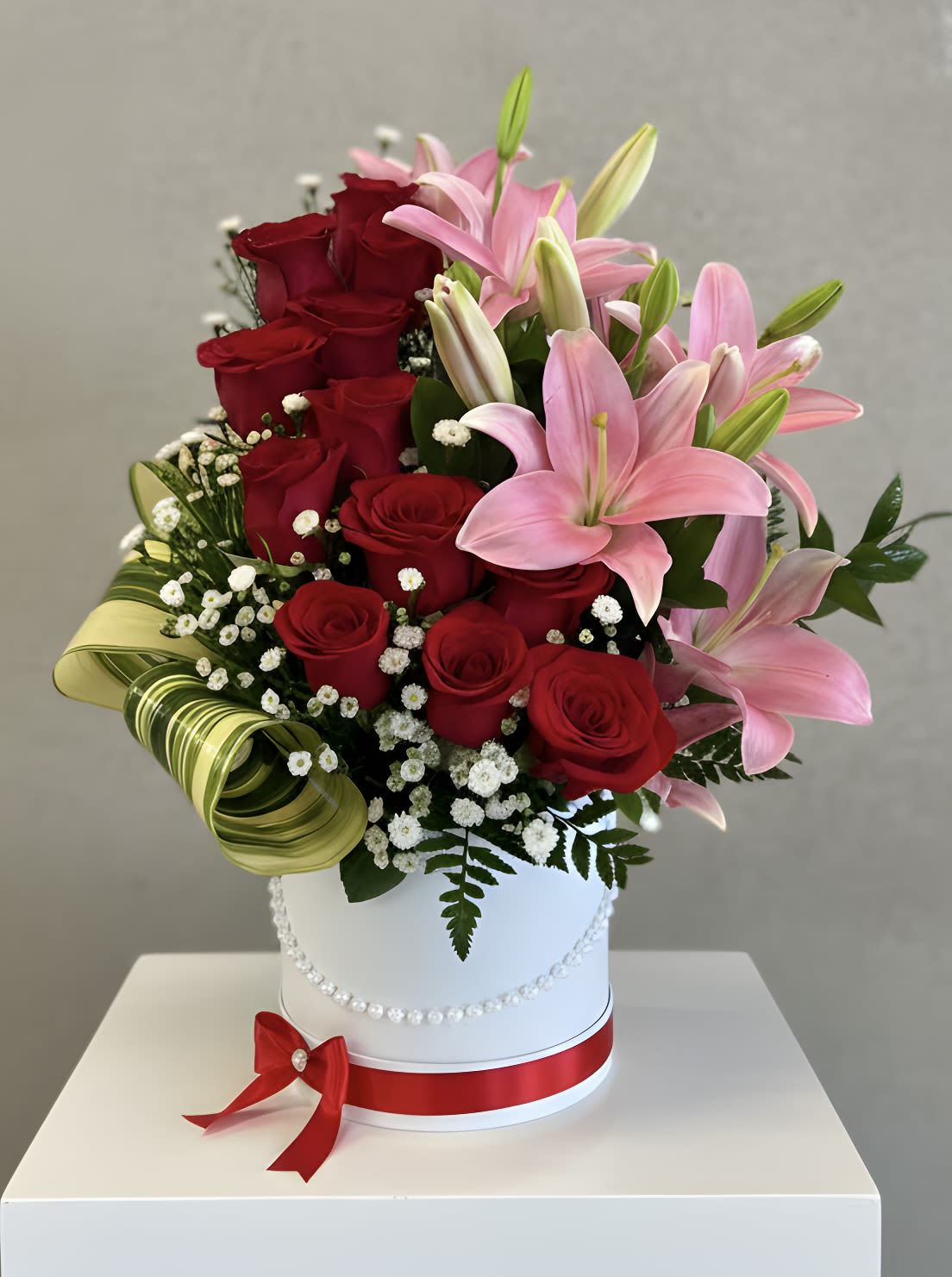 Red roses and pink lilies in a white hatbox with a red ribbon