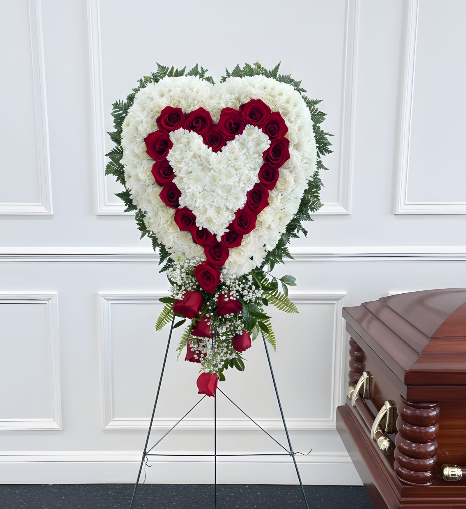 Heart-shaped funeral spray of white flowers and red roses beside a casket