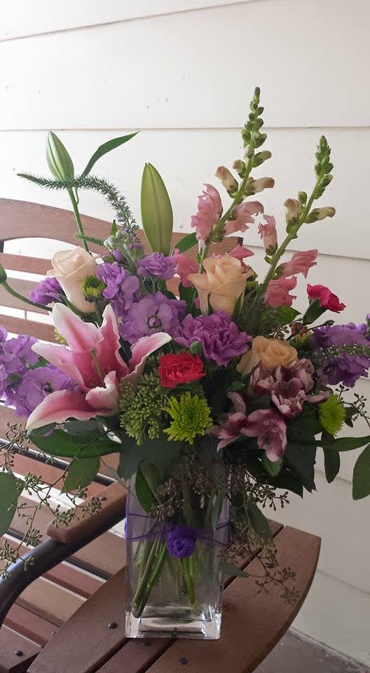 Mixed bouquet of pink, purple, and cream flowers in a clear glass vase