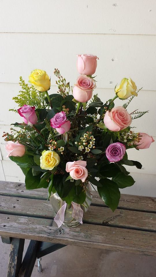 Mixed pastel roses arranged in a clear glass vase with a ribbon