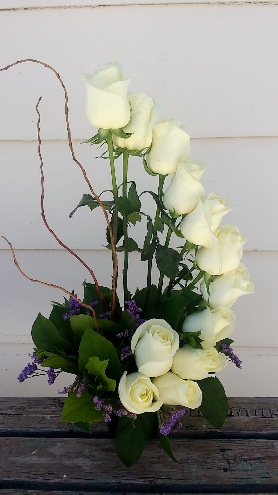 White roses arranged with purple filler in a low vase.